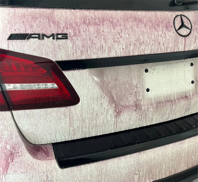 Iron-fallout remover bleeding red-violet as it dissolves embedded brake dust and contaminants on the rear of a Mercedes-AMG during a decontamination wash